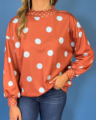 Rust polka dot long sleeve top with oversized light blue dots, contrasting mini dot mock neckline, cuffs and hem, and a relaxed fit.