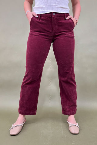 Person wearing maroon pants and a white top against a plain background