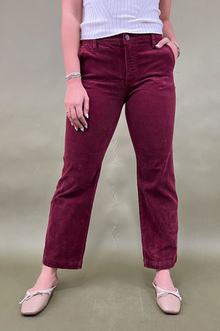 Person wearing maroon pants and a white top on a beige background