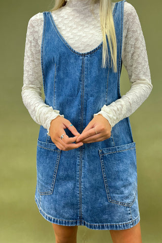 Person wearing a blue denim dress over a white long-sleeve shirt on a green background