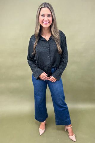 Woman wearing a black shirt and blue jeans against a green background