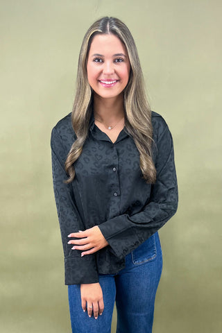 Woman wearing a black patterned shirt and blue jeans against a beige background