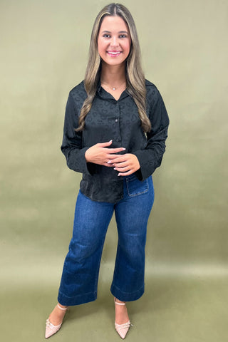 Woman wearing a black blouse and blue jeans against a green background