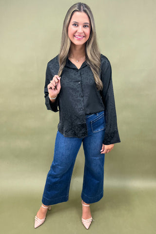 Woman wearing a black blouse and blue jeans against a green background