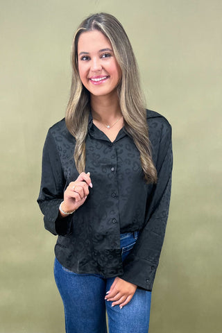 Woman wearing a black patterned shirt and blue jeans against a beige background