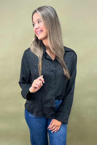Woman wearing a black patterned shirt and blue jeans against a beige background