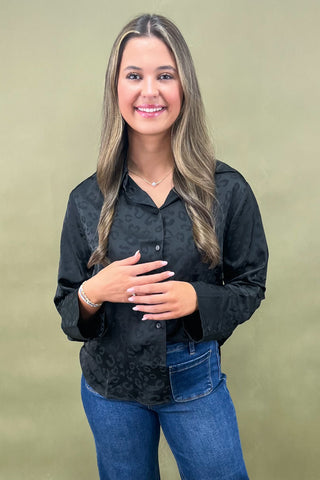 Woman wearing a black patterned shirt and blue jeans against a beige background