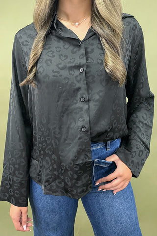 Person wearing a dark gray button-up shirt with a subtle pattern, paired with blue jeans on a light green background.