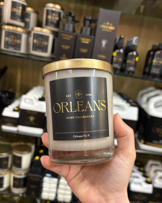 Hand holding a candle labeled 'Orleans' in front of a display of similar products.