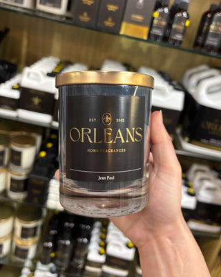 Hand holding a jar labeled 'Orleans Home Fragrances' in a store setting.