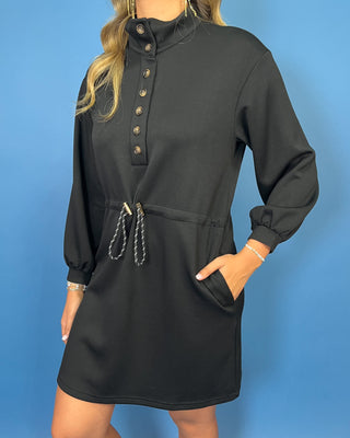 Black long sleeve mini dress with a buttoned mock neckline, adjustable drawstring waist, side pockets, and an easy sporty-chic silhouette.
