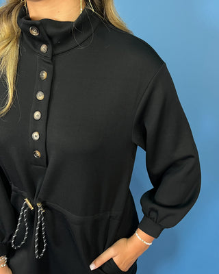 Black long sleeve mini dress with a buttoned mock neckline, adjustable drawstring waist, side pockets, and an easy sporty-chic silhouette.