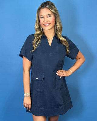 Navy short sleeve shift mini dress with a split neckline, relaxed silhouette, and front flap pockets with button details.