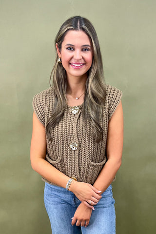 Woman wearing a brown knitted sleeveless top against a green background