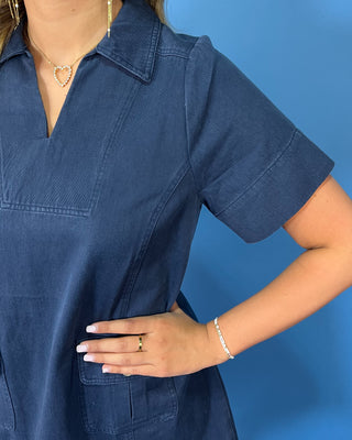 Navy short sleeve shift mini dress with a split neckline, relaxed silhouette, and front flap pockets with button details.