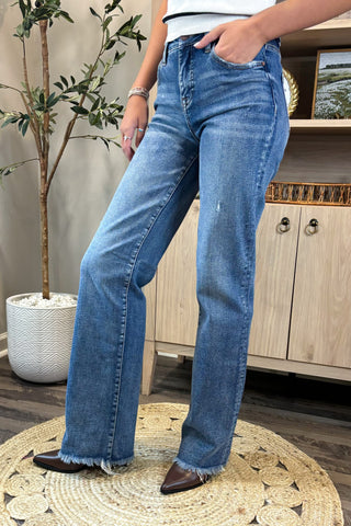 Person wearing blue jeans standing on a round woven mat indoors.