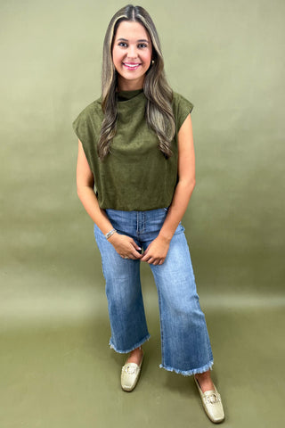 Woman wearing an olive green sleeveless top and blue jeans against a green background