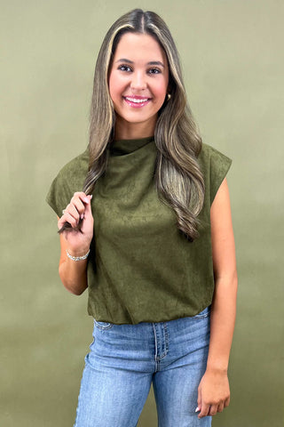 Woman wearing an olive green top and blue jeans against a green background