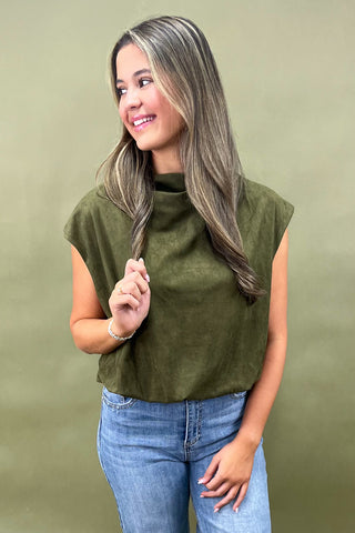 Woman wearing an olive green sleeveless top and blue jeans against a beige background