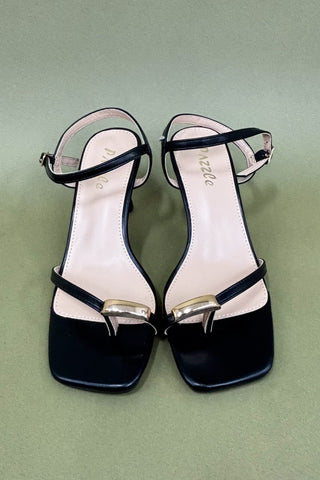Black high-heeled sandals with gold accents on a green background