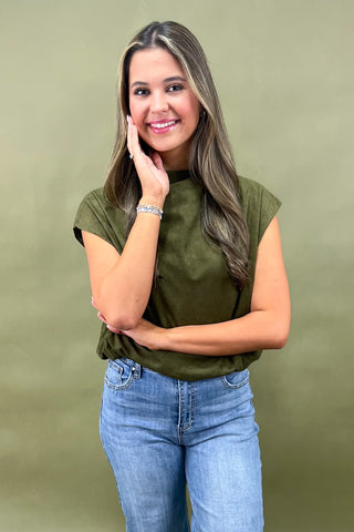 Woman wearing an olive green top and blue jeans against a green background