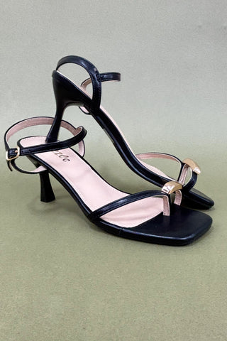 Black high-heeled sandals with thin straps on a light green background
