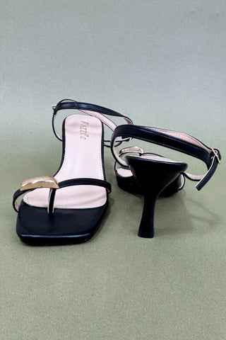 Black high-heeled sandals with a visible brand name on a light green background