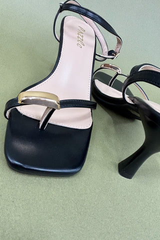 Black high-heeled shoes with gold accents on a light green background