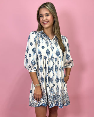 Woman wearing a white dress with blue patterns on a pink background
