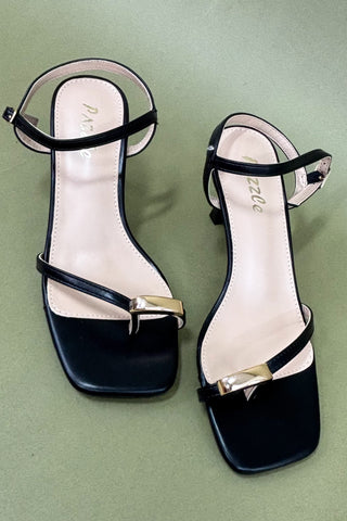Black high-heeled sandals with gold buckles on a green background