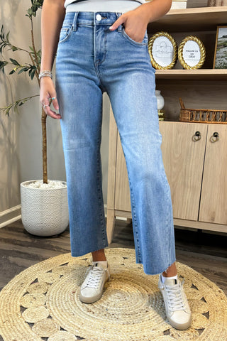 Person wearing blue jeans and white sneakers standing on a textured rug with a wooden cabinet in the background.