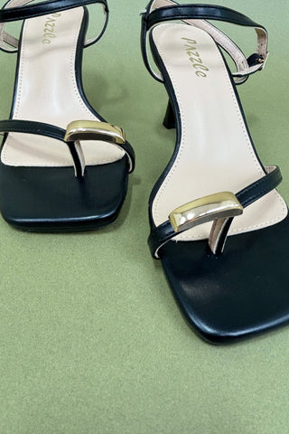 Black high-heeled sandals with gold straps on a green background