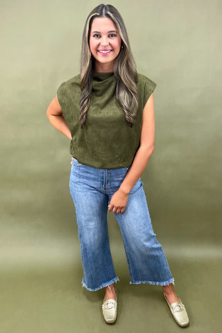 Woman wearing an olive green sleeveless top and blue jeans against a green background