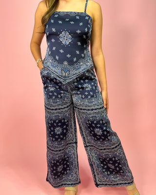 Person wearing a navy blue patterned jumpsuit on a pink background