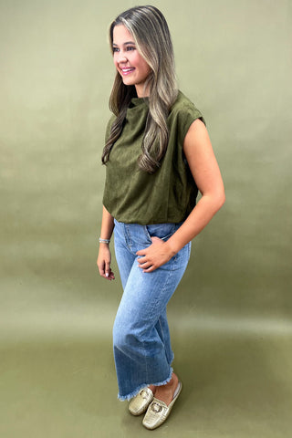 Woman wearing an olive green top and blue jeans on a green background