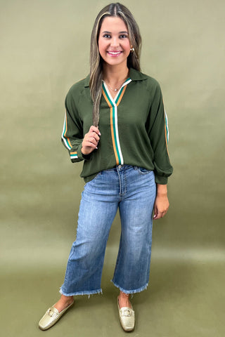 Woman wearing a green sweater with striped sleeves and blue jeans against a beige background