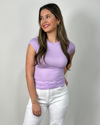 Model wearing a lavender fitted short sleeve tee with high-waisted white cropped pants, styled with clear slide sandals.