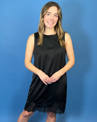 Black sleeveless satin shift dress with a classic round neckline, relaxed silhouette, and delicate lace trim along the hem.