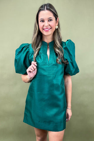 Woman wearing a green dress with puffed sleeves against a beige background