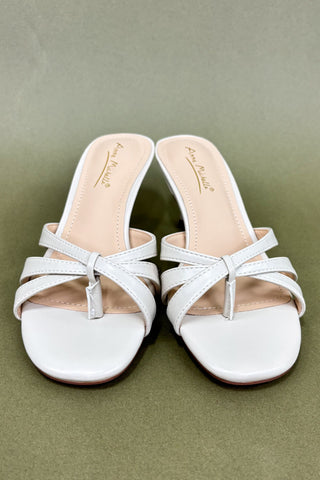 Pair of white sandals with thin straps on a green background
