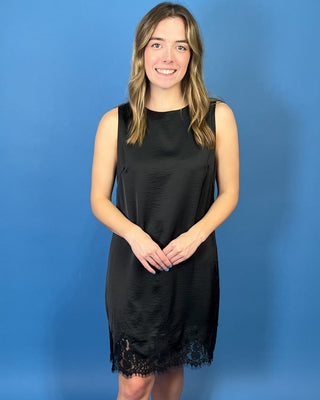 Black sleeveless satin shift dress with a classic round neckline, relaxed silhouette, and delicate lace trim along the hem.