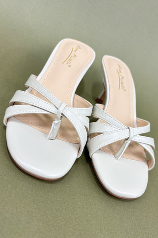 Pair of white sandals with thin straps on a green background
