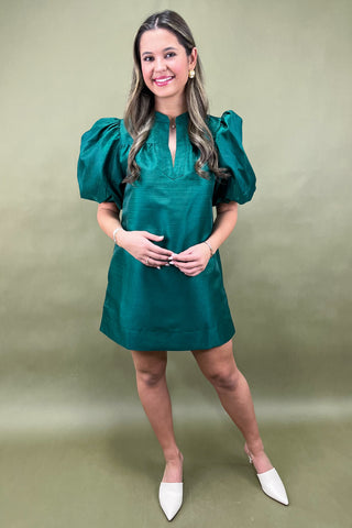 Woman wearing a green dress with puffed sleeves against a beige background