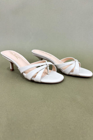 Pair of white high-heeled sandals on a green background