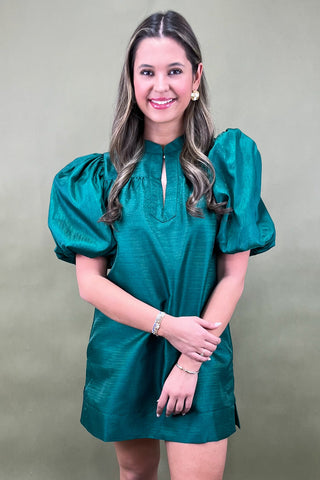 Woman wearing a green dress with puffed sleeves against a beige background