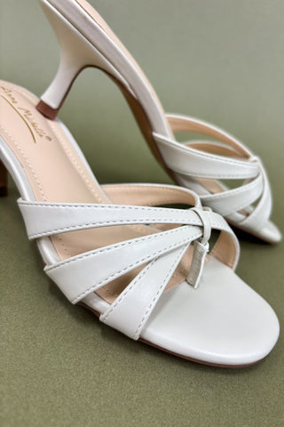 White high-heeled sandals with criss-cross straps on a green background