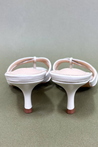 Pair of white high-heeled shoes with pink soles on a light gray background
