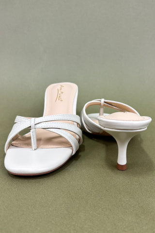 White high-heeled sandals on a green background