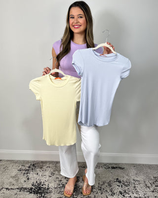 Model wearing a lavender fitted short sleeve tee with high-waisted white cropped pants, styled with clear slide sandals.