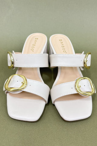 White sandals with gold buckles on a green background